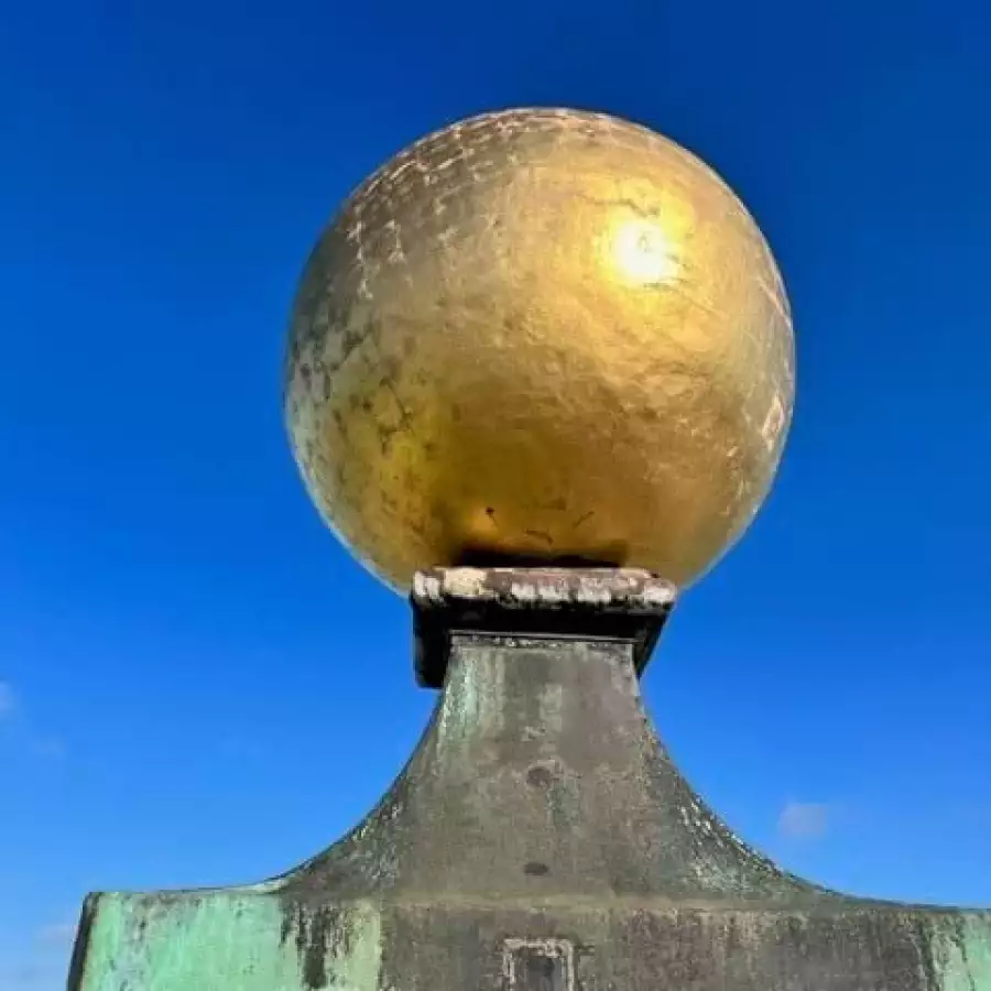 A gilded ball gleams on top of a weathered green copper finial against a deep blue sky