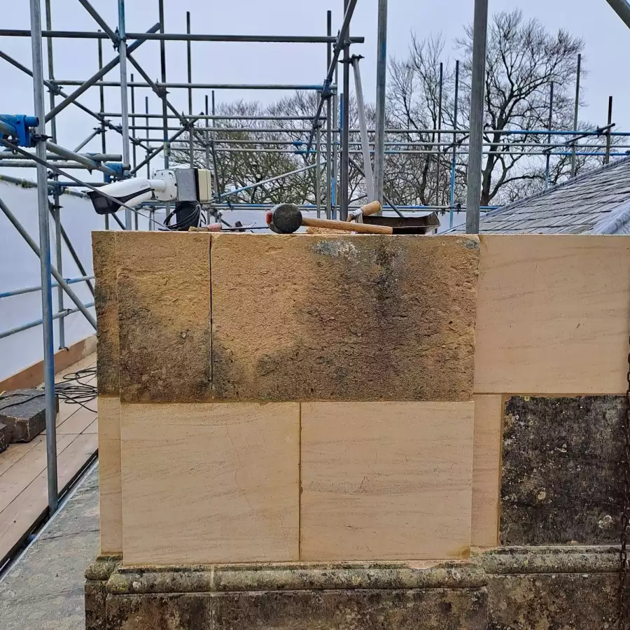 New pale stone blocks set into weathered stonework at the top of a wall, surrounded by scaffolding