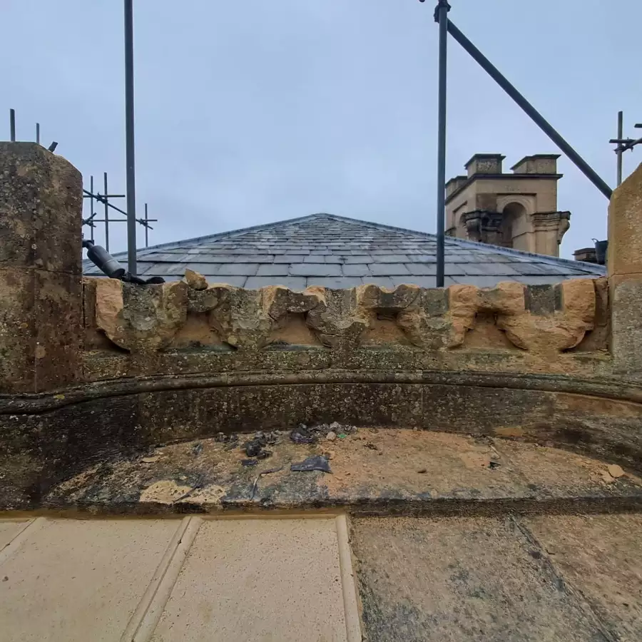 Weathered stone battlements and a slate roof, seen through scaffolding